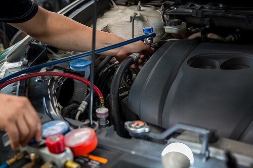 Air Conditioning/Heating Service in Queen Creek, AZ | Ace Performance Auto. Closeup image of an auto mechanic checking and fixing a car’s air conditioner system in a car garage. 