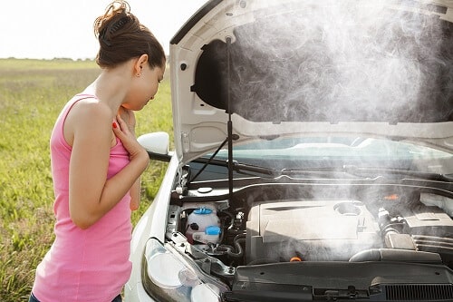 What to do with Engine Overheating | Ace Performance Auto in Queen Creek, AZ. Image of a frustrated young woman looking at the overheated engine of her car on the road.