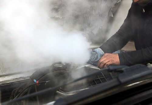 Cooling System Service in Gilbert, and Queen Creek, AZ | Ace Performance Auto. Image of a man mechanic repairing a smoking engine of an overheated car.